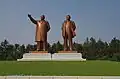 3/4 Statues of Kim Il-sung and Kim Jong-Il (artwork_type=statue and tourism=artwork) in bronze on their square base seen from the ground.