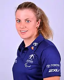 A blonde haired woman wearing her hair in a ponytail, and wearing a blue polo shirt