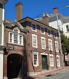 A color photograph of buildings along Thomas Street in Providence, Rhode Island. The brick Seril Dodge House at right has three stories. It has a large wooden door, over which a lamp hangs. A small iron sign saying "Providence Art Club" hangs from side of the building, over the sidewalk. A small brick archway connects it to the other Seril Dodge House at left, just out of view.