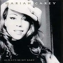 A black-and-white photo of Carey smiling from the song's remix video, sporting a long wavy hairstyle and wearing a large hat.