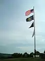 (Top down) American, New York State, Prisoner of War and New York State Office of Parks Recreation and Historic Preservation flags fly atop the hill at the battlefield