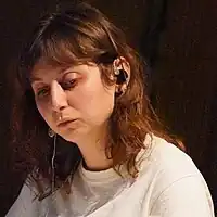 Portriat photo of a young brunette woman in a white shirt looking downwards