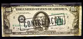 An overprinted Series 1974 counterfeit $100 bill, marked 'Contrefaçon' (counterfeit in French) to indicate its status as a fake