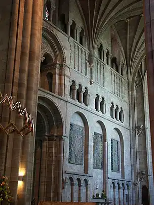  A transept interior with a wall panelled with shallow Norman arches and open galleries.