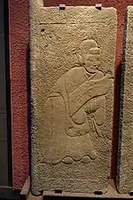 An Eastern Han carved stone tomb door showing a man carrying a shield, wearing a long robe with apron and a wuguan (武冠), stored in Sichuan Provincial Museum in Chengdu.