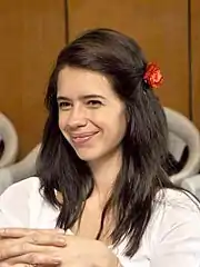 Koechlin in a white dress smiling at the camera