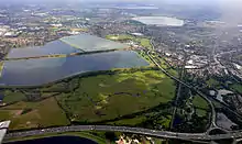 Image 9Seven reservoirs. View of four in Spelthorne with small lakes of lower elevation, from aggregate extraction, in the south of the borough to the right. Beyond three reservoirs in Elmbridge. The flattest areas of the far north of the county. Staines road and rail bridges span the Thames into Runnymede in the right of the photograph. (from Portal:Surrey/Selected pictures)