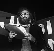 Herman Schiller standing behind a microphone in front of a banner