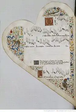 Medieval manuscript leaf shaped like a heart. It bears 5 musical staves: the 3rd is empty, the 4th is filled with lyrics, the rest are filled with musical notation in black ink with lyrics below. The lyrics open with enlarged initials in gold on painted squares. Surrounding the staves are decorative borders in gold and colours consisting of blocks of curling vines from which spring leaves and flowers. Cavorting among the foliage are a large bird, a monkey wearing a red hat while reading a book, and a 4-legged monster with a snake-like neck and the face of a lion.