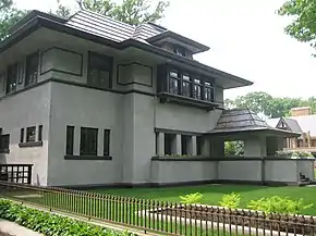 Recent exterior view of the house from the southeast corner. The library windows are visible at left with the entrance porch at far right. The living room planter with bedroom bay window are at center. Deep eaves shade the house from the mid-day summer sun.