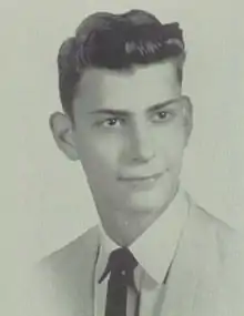 A black-and-white bust-length photo of a young white man in a light-colored suit and tie