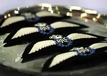 Four RAF badges in a row, each showing letters RAF, inside a blue laurel, with a crown above it and wings to either side