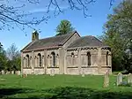 A stone church with a semi-circular chancel and a small bell-cot