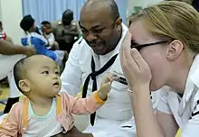 US Navy 100406-N-7478G-346 Operations Specialist 2nd Class Reginald Harlmon and Electronics Technician 3rd Class Maura Schulze play peek-a-boo with a child in the Children's Ward at Hospital Likas