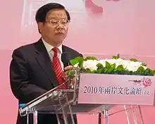 a serious looking man with a wavy haircut, wearing glasses, a white shirt, a suit and a red tie with white stripes