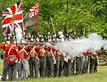 Re-enactors (in UK uniforms) fire muskets toward the "Americans" in annual commemorations