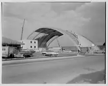 The Island Garden arena construction site in 1956. A large, vaulted frame — reminiscent of an airplane hangar — has half its ceiling assembled.